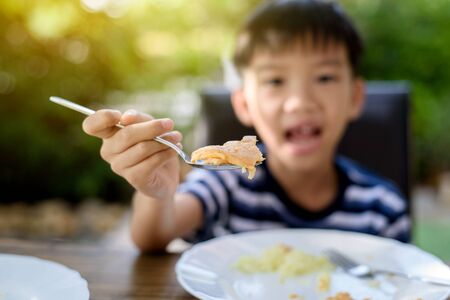 Selective focus at Young Thai boy eating with food on the wooden table with his family in the garden. And out focus tree background.の写真素材