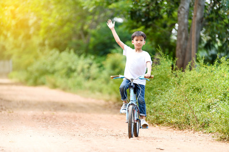Young Thai boy ride bicycle and wave his hand on the road in the park.の写真素材