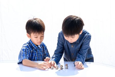 Young happy Thai boy build a tower by a coin on white backgroundの写真素材