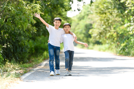 Two young Thai boy walk and wave his hand in the park.の写真素材