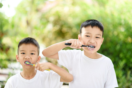 Selective focus at two young Asian boy brushing his teeth in the home garden with out focus green plant background.の写真素材