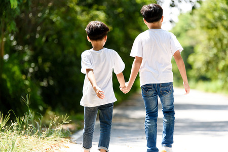 Two young Thai boy run together on the crack road in the natural park.の写真素材