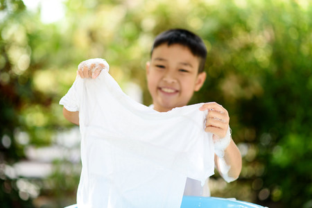 Selective focus at shirt that washing by young Thai little boy at the home garden with out focus green plant.の写真素材