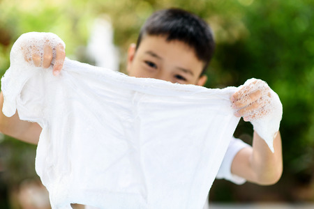 Selective focus at shirt that washing by young Thai little boy at the home garden with out focus green plant.の写真素材