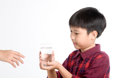 Young Thai boy drinking fresh water from glass on white backgroundの写真素材