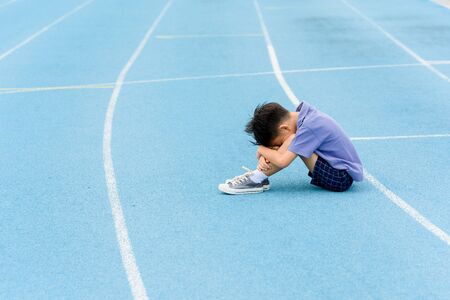 Selective focus at young Asian boy sit and tired on blue track after running.の写真素材