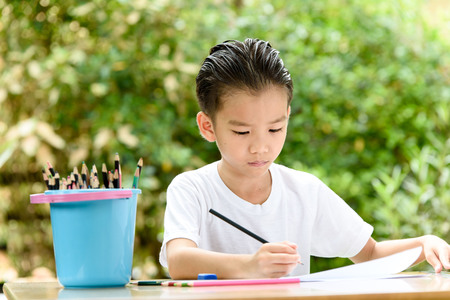 Young Asian boy write on the note book by color pencil in the gardenの写真素材