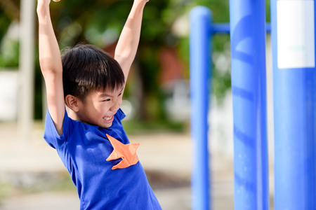 Young asian boy hang the yellow bar by his hand to exercise at out door playgroundの写真素材