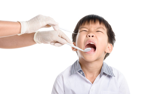 Dentist checking young asian boy teeth by equipment on white background.の写真素材