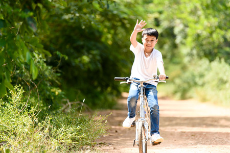 Young Thai boy ride bicycle and wave his hand on the road in the park.の写真素材