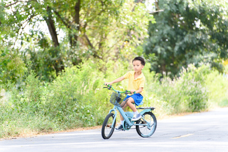 Young Asian boy ride a blue bicycle on the old road beside the tree and grass in summer time with warm sunlight.の写真素材