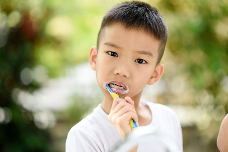 Selective focus at young Asian boy brushing his teeth in the home garden with out focus green plant background.の写真素材