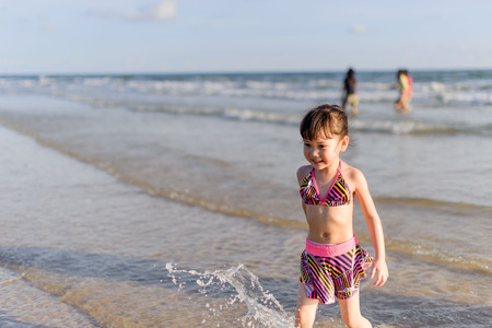 Young Thai girl play on the sand beach next to the tropical sea.の写真素材