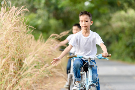 Young Asian Thai boy riding bicycle in the park and touch flower of grass with family.の写真素材