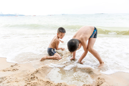 Two young Asian Thai boy playing on the sand beachの写真素材