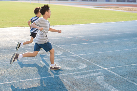 Young Asian boy running on blue track in the stadium during day time to practice himself.の写真素材