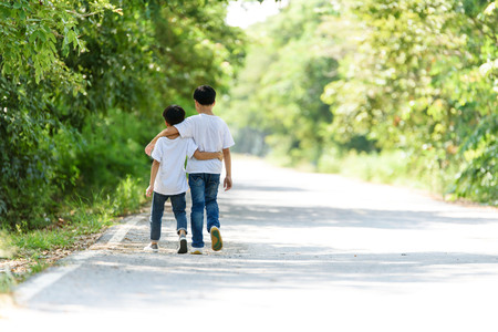 Two young Thai boy run together on the crack road in the natural park.の写真素材