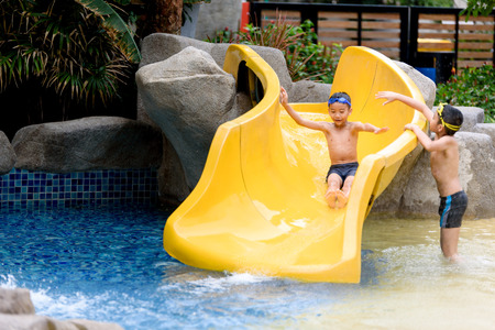 Young Asian Thai boy play water slider in a park during summer time.