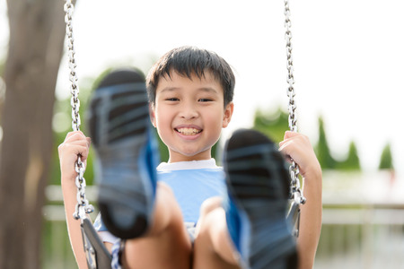 young asian boy play a iron chain swinging at the playground under the sunlight in summerの写真素材