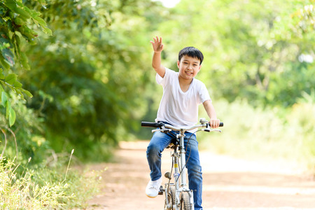 Young Thai boy ride bicycle and wave his hand on the road in the park.の写真素材