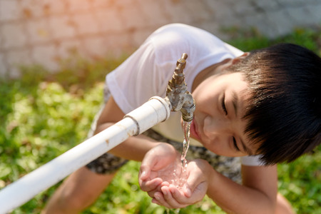 Close up young asian boy taking water from old faucet in the garden. Water shortage and drought conceptの写真素材
