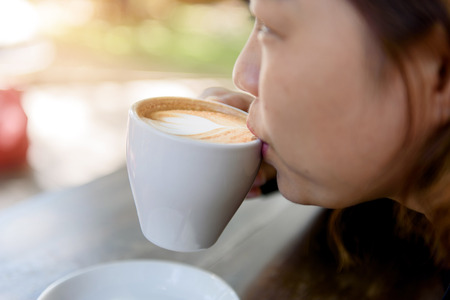 Selective focus at woman take cup of coffee latte with heart pattern in a white cup on old wooden table.の写真素材