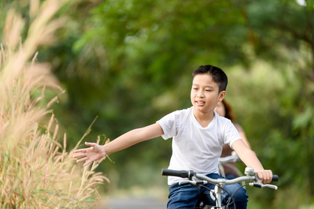 Young Asian Thai boy riding bicycle in the park and touch flower of grass with family.の写真素材
