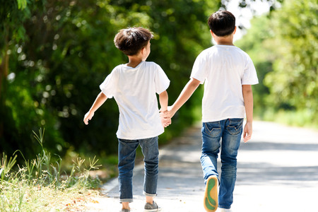 Two young Thai boy run together on the crack road in the natural park.の写真素材