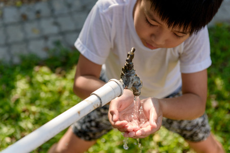 Close up young asian boy taking water from old faucet in the garden. Water shortage and drought conceptの写真素材