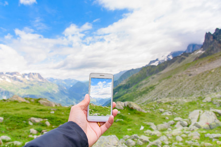 Hand holding smartphone taking photo of Aiguile du Chardonnet a beautiful view of Mont Blanc Massif , Chamonix France, Europeの写真素材
