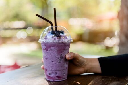Selective focus at Blueberry smoothie in a take home cup with straw in woman hand.の写真素材