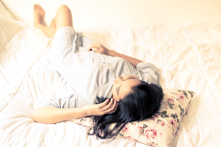 Vintage color tone. Selective focus on young Asian girl face lay on the flower pillow and white bed...