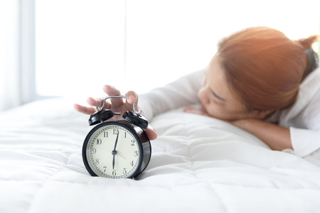 Selective focus at vintage black alarm clock morning time and out focus at young girl sleep on the...