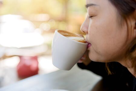Selective focus at woman take cup of coffee latte with heart pattern in a white cup on old wooden table.の写真素材
