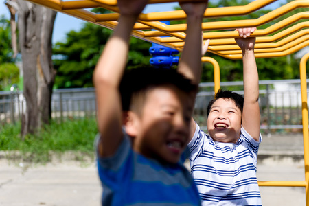 Happy Young asian boy hang the yellow bar by his hand to exercise at out door playground under the strong sunlight in summer time.の写真素材