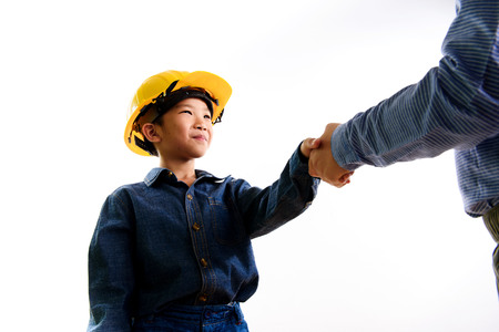 Young asian Thai boy in yellow safety helmet pretend to be engineering during construction area shaking hand to be success.の写真素材