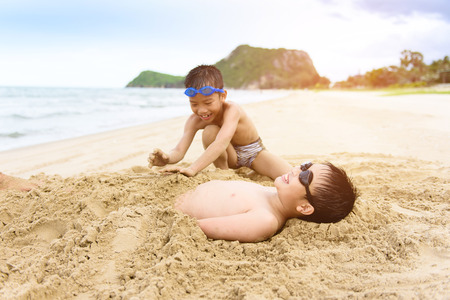 Young Asian Thai boy play with a sand bed on the beach during summerの写真素材