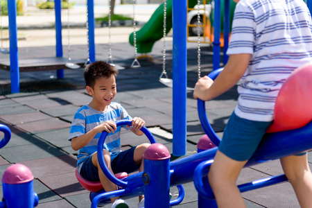 Happy Two young asian boy play on the balance bar at outdoor playground under the strong sunlight in summer time.の写真素材