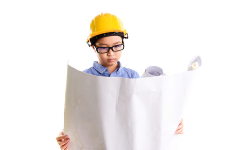 Young asian Thai boy in yellow safety helmet pretend to be engineering during construction area are looking in the drawing paper.の写真素材