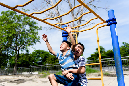 Happy Young asian boy hang the yellow bar by his hand to exercise at out door playground under the strong sunlight in summer time.の写真素材