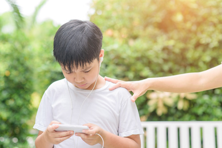 Young Asian Thai boy using a smartphone to play game and listen to music without care the surrounding.の写真素材
