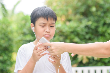 Young Asian Thai boy using a smartphone to play game and listen to music without care the surrounding.の写真素材
