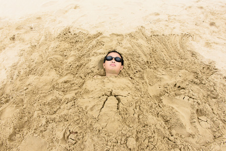 Young Asian Thai boy play with a sand bed on the beach during summerの写真素材
