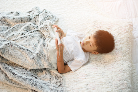 Preteen Asian Thai boy using a smartphone to play game and listen to music without care the...