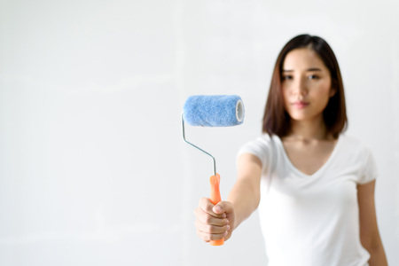 Selective focus at painting roller in young Asian woman hand in front of a reparing old wall in a bed room.の写真素材