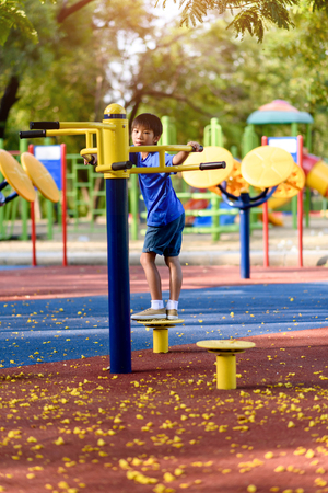 Young Asian boy play a swing in a public playgroun in a park.の写真素材