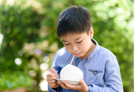 Young Asian Thai boy drink a fresh juice from ready to drink coconut that remove all hard cover from the soft white skin during summer.の写真素材