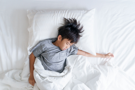 Young Asian boy sleeping on a white bedの写真素材