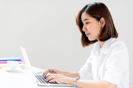 Young happy Asian woman working in a white office with laptop.の写真素材
