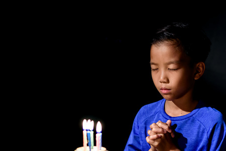 Young Asian boy celebrate and blow the candle of his birthday cake in a dark room.